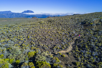 France, Reunion island (French overseas department), Reunion National Park listed as World heritage by UNESCO, on the slopes of the Piton de la Fournaise volcano, hiker on the Ste Therese oratory trail above the Plaine des Sables, the Piton des Neiges in the background to the north (aerial view)