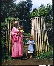 Burundi, Bujumbura Province, Ijenda area, young Tutsi mother and her children in front of main courtyard of the rugo (traditional farm) and the livestock enclosur, the main entry may be blocked quickly with branches placed next to the door (4x5 reversal film reproduction)