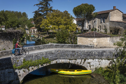 France, Charente (16), Bassac, cycliste faisant la véloroute La Flow Vélo passant le pont sur la Guirlande, un petit affluent du fleuve La Charente qui traverse le pied du bourg (vue aérienne)