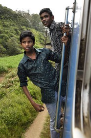 Sri Lanka, Uva Province, the popular scenic train ride through the tea growing hill country between Hatton and Ella, young passengers hanging outside the door of the moving train around Ambewela