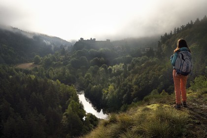 France, Haute Loire, Loire river Valley, Arlempdes, labelized the Most Beautiful Villages of France, hiker observing the ruins of the castle perched on a basalt rock overlooking a Loire river meander