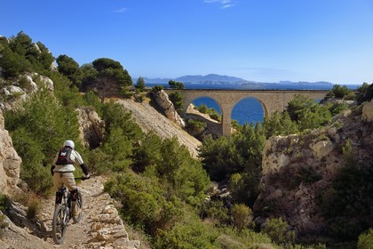 France, Bouches du Rhone, Le Rove towards Marseille, the Cote Bleue (Blue Coast), hike from Niolon to Cap Méjean along the Customs Trail, mountain biker descending to the Jonquier calanque railway bridge and the archipelago of Frioul islands in the background