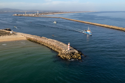 Portugal, Algarve, Ria Formosa Natural Park, Faro, Island of Barreta or Deserta (Ilha da Barretta or Deserta) fishing boat leaving the port, the lighthouse of Ilha do Farol part of Ilha da Culatra in the background (aerial view)