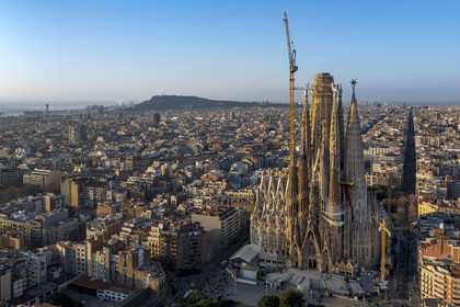 Spain, Catalonia, Barcelona, Eixample district, Sagrada Familia basilica by Catalan modernist architect Antoni Gaudi, listed as a UNESCO World Heritage Site, facade of the Nativity, the port and Montjuic hill in the background