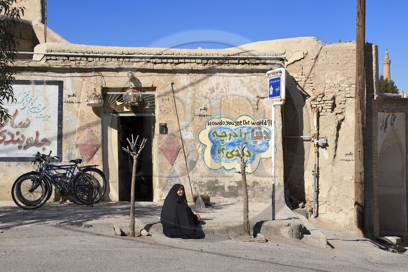 Iran, Province d'Ispahan, désert du Dasht-e Kavir, ville de Nain ou Na'in, femme devant une maison avec un graffiti affichant comment voyez vous le monde