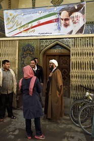 Iran, Isfahan Province, Isfahan, mullah in the Bazar-e Bozorg (Great Bazaar), a massive covered bazaar which dates back almost 1300 years, Mullah at the entrance of a madrassa and under a poster honoring both the Revolution guides Ayatollah Khomeini and Ayatollah Khamenei (right)