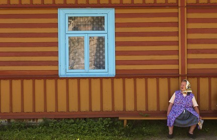 Poland, Lesser Poland, Carpathian Mountains, country woman sitting in front of her wooden painted house in the village of Debno