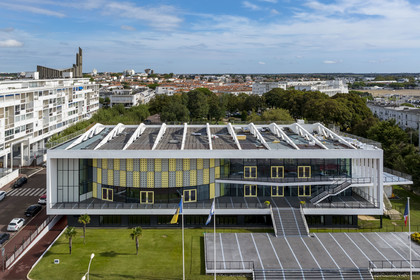 France, Charente-Maritime (17), Royan, le Palais de congrès (1957) signé de l’architecte-urbaniste Claude Ferret et rythmés par les panneaux perforés en aluminium jaune et gris des ateliers Jean Prouvé en façade, l'église Notre-Dame de Royan construite de 1955 à 1958 par l'architecte Guillaume Gillet en arrière plan (vue aérienne)