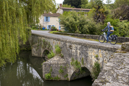 France, Vendée (85), Vouvant, labellisé Les Plus Beaux Villages de France, cycliste traversant le petit pont médiéval sur la rivière La Mère qui entoure le village