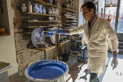 France, Nièvre, Nevers, Fayencerie d’art de Nevers, master earthenware maker Clair Bernard dips the biscuit using a metal claw into the Bleu de Nevers enamel bath