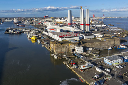 France, Loire-Atlantique (44), Saint-Nazaire, l’écluse Est et l'écluse fortifiée de l'ancienne base sous-marine allemande construite lors de la dernière guerre mondiale au premier plan et le chantier du super-yacht de luxe Ritz-Carlton Luminara dans la forme Joubert, les tours d'éoliennes en arrière plan sont stockées avant embarquement (vue aérienne)