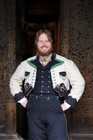 Norway, Oslo, Bygdoy Peninsula, Norsk Folkemuseum (Norwegian Folk Museum), man with tradional Sunday best oufit of a 19th century Telemark farmer in front of Gol Stave Church