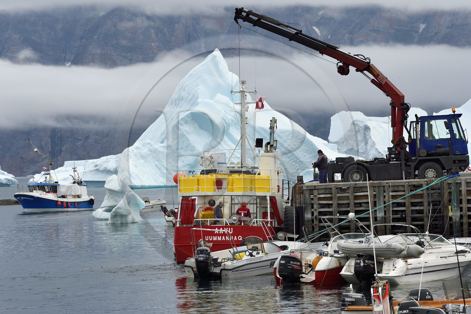 Groenland, cote ouest, Uummannaq, bateau de pêche déchargeant dans le port et icebergs en arrière plan