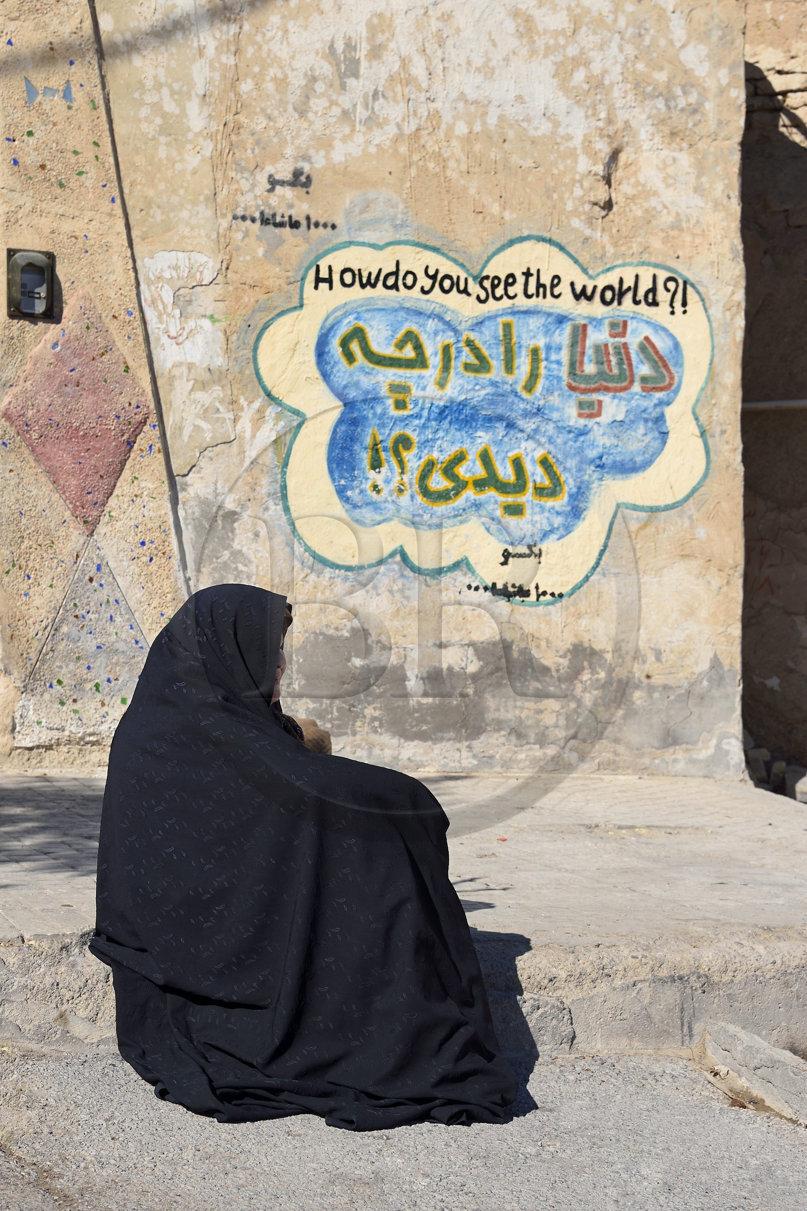 Iran, Province d'Ispahan, désert du Dasht-e Kavir, ville de Nain ou Na'in, femme devant une maison avec un graffiti affichant comment voyez vous le monde