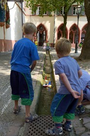 Germany, Baden-Wurttemberg, Freiburg im Breisgau, Rathausplatz, children playing with small boats in one of the Bächle which are small open channel lining the sidewalks