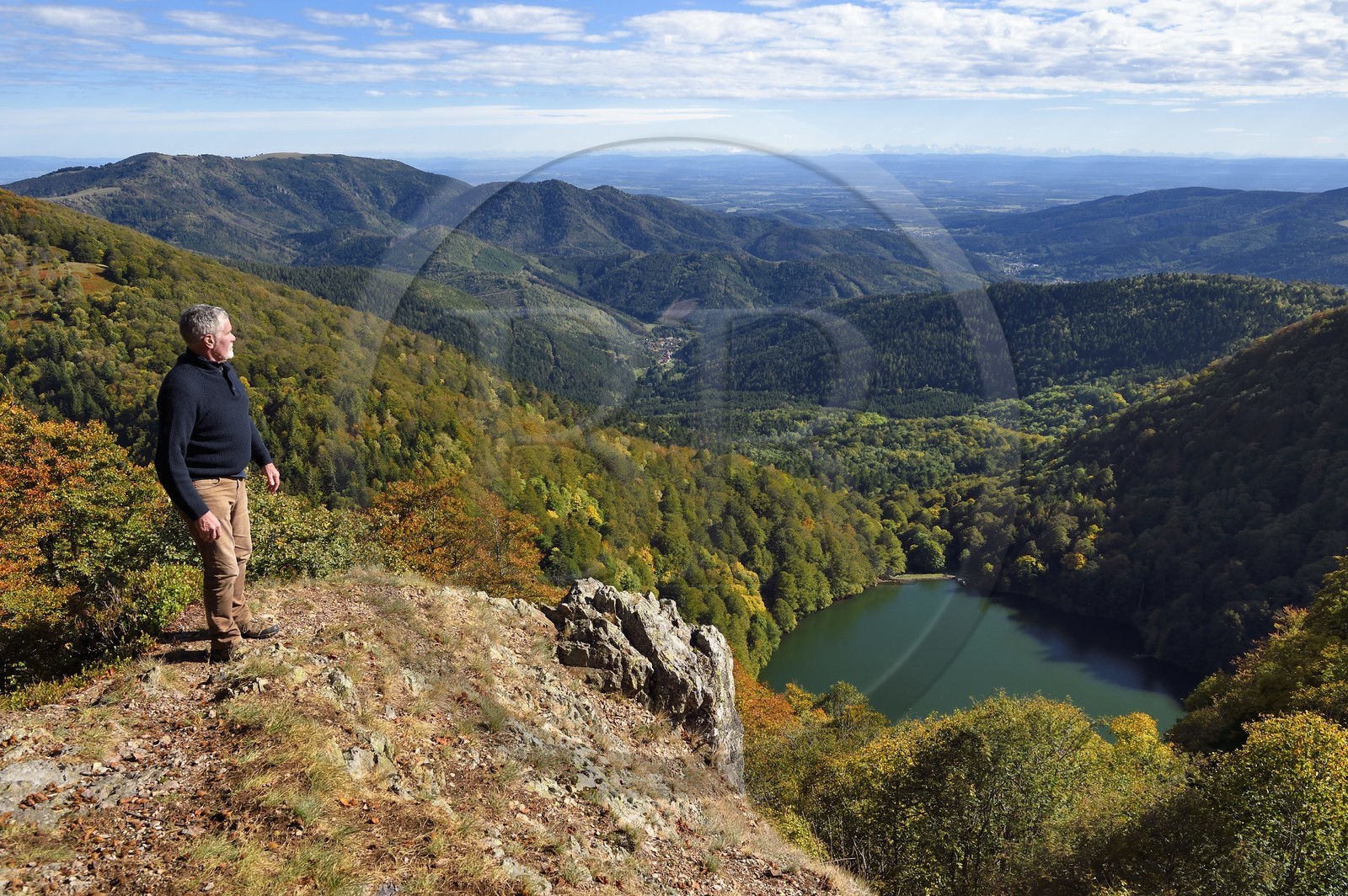 France, Vosges (88), Parc naturel régional des ballons des Vosges, Saint-Maurice-sur-Moselle, randonneur au sommet de la Tete des Perches au dessus de Gazon Rouge, le Lac des Perches, la plaine d'Alsace et les Alpes en arrière plan