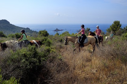 France, Var, Agay area next to Saint-Raphael, riders trekking in the Massif de l'Esterel (Esterel Massif) and the Ile d'Or island on the Dramont cape in the background