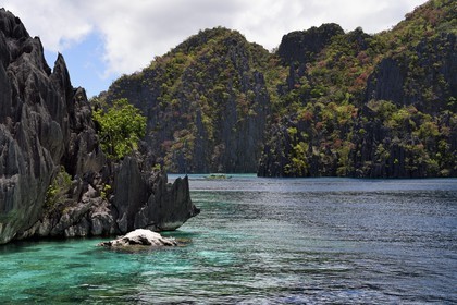 Philippines, Calamian Islands in northern Palawan, Coron Island Natural Biotic Area, Outrigger canoe in a lagoon under Permian Limestone of Jurassic origin cliffs