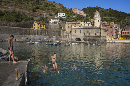 Italie, Ligurie, Cinque Terre, parc national des Cinque Terre classé Patrimoine Mondial de l'UNESCO, village de Vernazza, jeunes gens plongeant dans le port et l'église paroissiale de Sainte Marguerite d'Antioche (Santa Margherita) flanquée d'un haut clocher octogonal