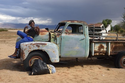 Namibie, région de Khomas, désert du Namib à l'Est du parc national Namib Naukluft, station essence de Solitaire, Gloria une jeune routarde namibienne qui fait la route assise sur la carcasse d'un pick-up Chevrolet