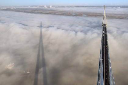 France, entre Calvados (14) et Seine-Maritime (76), cargo passant sous le Pont de Normandie qui émerge des brumes matinales de l'automne et enjambe la Seine, la Réserve Naturelle de l'estuaire de la Seine en arrière plan, vue depuis le sommet du pylone sud