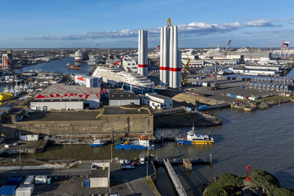 France, Loire-Atlantique (44), Saint-Nazaire, l’écluse Est et l'écluse fortifiée de l'ancienne base sous-marine allemande construite lors de la dernière guerre mondiale au premier plan et le chantier du super-yacht de luxe Ritz-Carlton Luminara dans la forme Joubert, les tours d'éoliennes à droite sont stockées avant embarquement, le paquebot de 333m MSC World America construit par les Chantiers de l'Atlantique en arrière plan (vue aérienne)