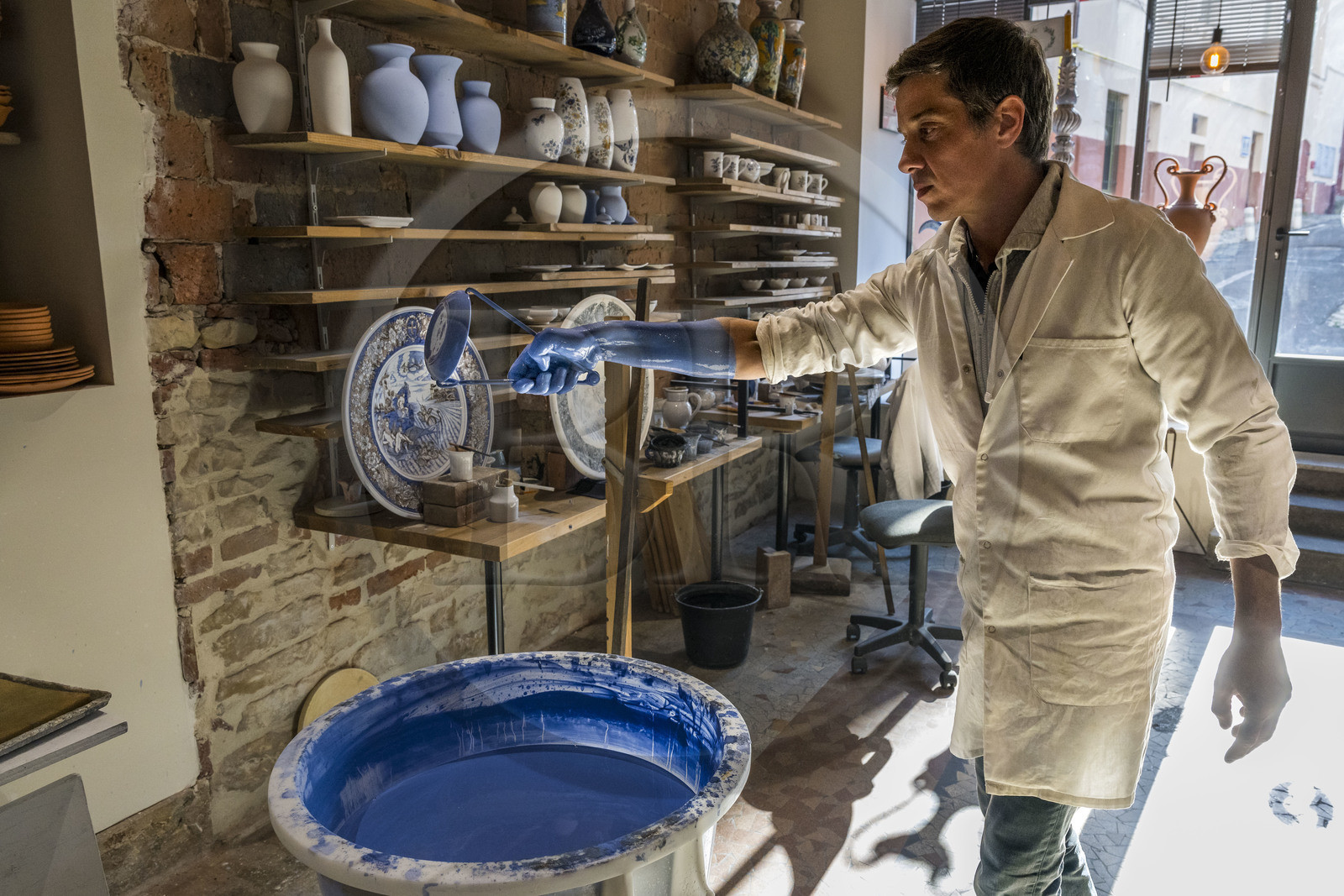 France, Nièvre (58), Nevers, Fayencerie d’art de Nevers, le maître faïencier Clair Bernard trempe le biscuit à l'aide d'une griffe métallique dans le bain d'émail Bleu de Nevers
