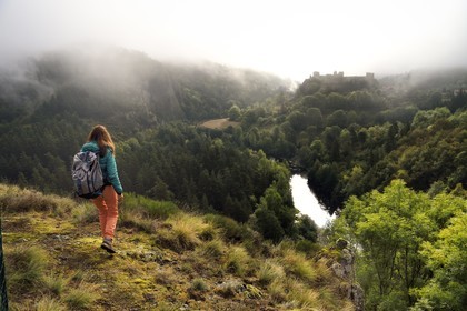 France, Haute Loire, Loire river Valley, Arlempdes, labelized the Most Beautiful Villages of France, hiker observing the ruins of the castle perched on a basalt rock overlooking a Loire river meander