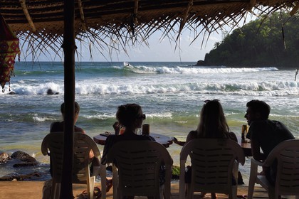 Sri Lanka, Province du Sud, Matara (district), Weligama, plage de Mirissa, jeunes gens attablés dans un restaurant de plage observant un surfeur