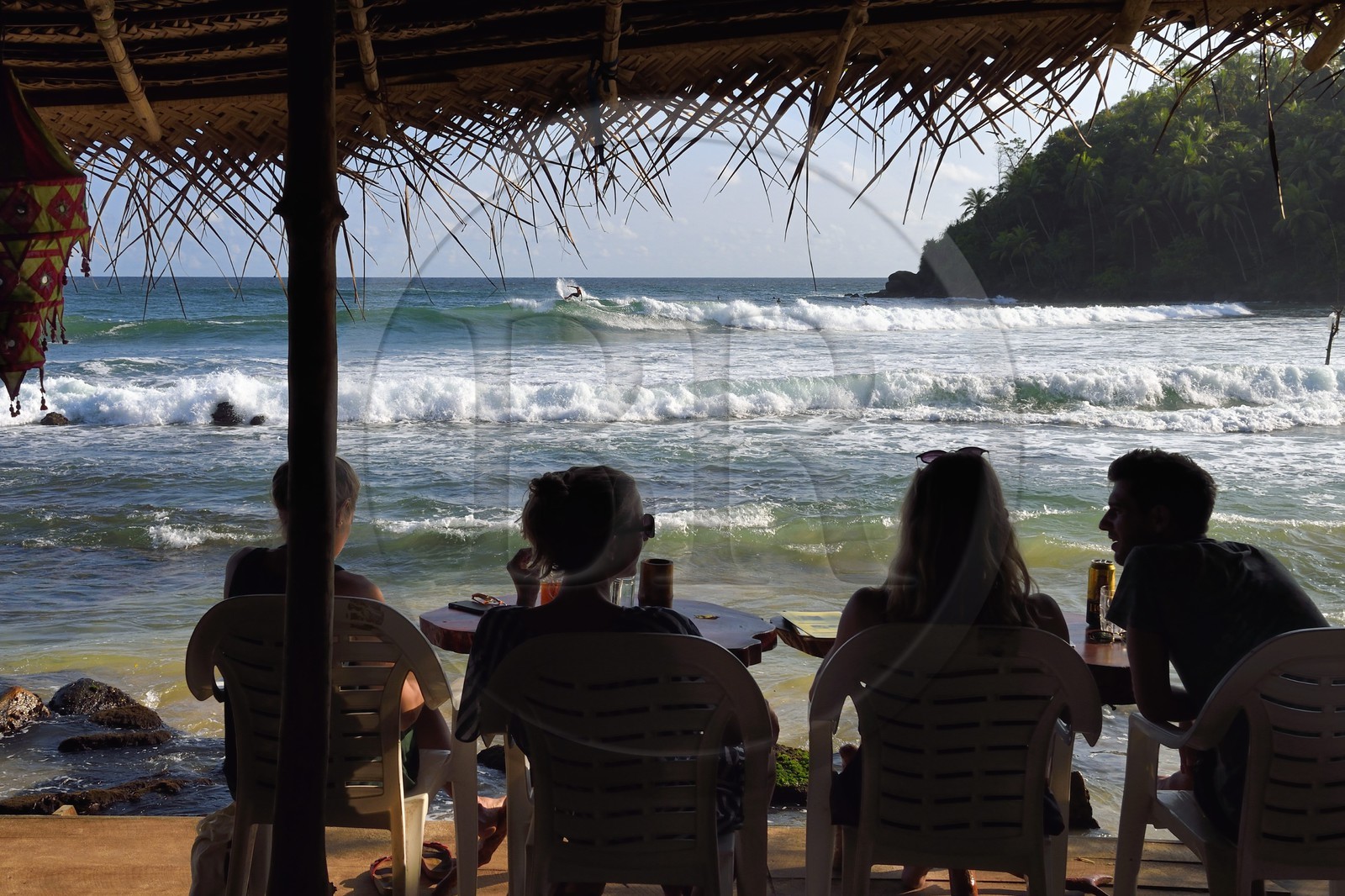 Sri Lanka, Province du Sud, Matara (district), Weligama, plage de Mirissa, jeunes gens attablés dans un restaurant de plage observant un surfeur