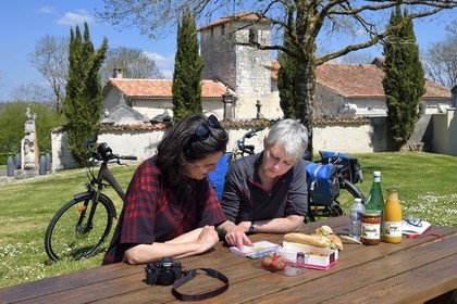 France, Charente (16), Souffrignac, pique-nique de cyclistes sur la véloroute la Flow Vélo aux Jardins du Bandiat, l'église romane Saint-Antoine du XIIème siècle en arrière plan