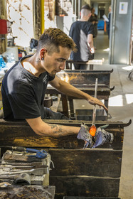France, Moselle, Meisenthal, Centre international d'Art verrier (CIAV) (international glass centre), the blowing workshop, the glassmaker Nicolas regulates the mass at home plate while performing a continuous rotation of his cane and preparation of the parison before passing to the mold