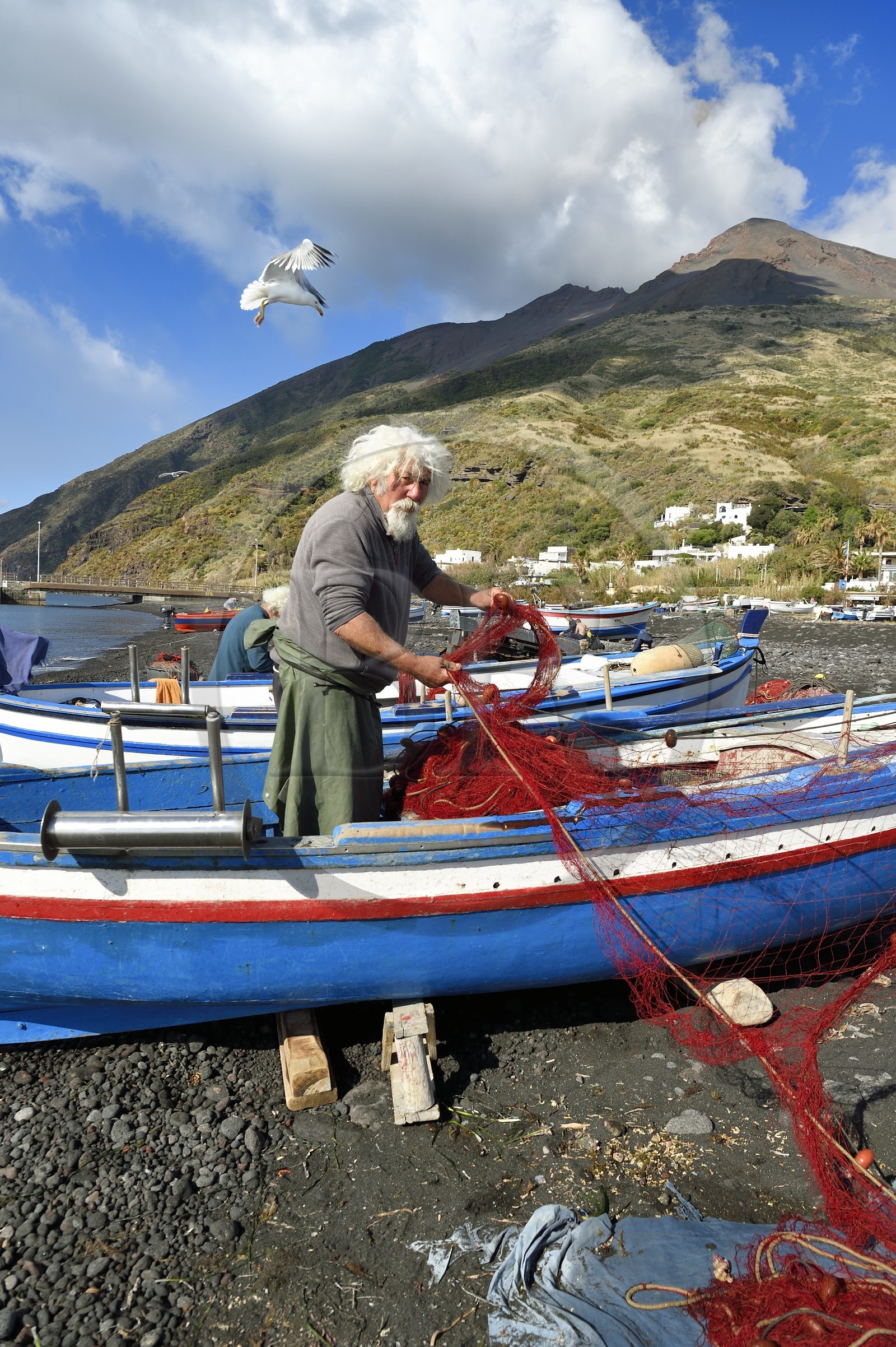 Italie, Sicile, iles Eoliennes, classées Patrimoine Mondial de l'UNESCO, ile de Stromboli, le pecheur Gaetano Cusolito réparant ses filets sur la plage de Scari et le volcan du Stromboli en arrière plan