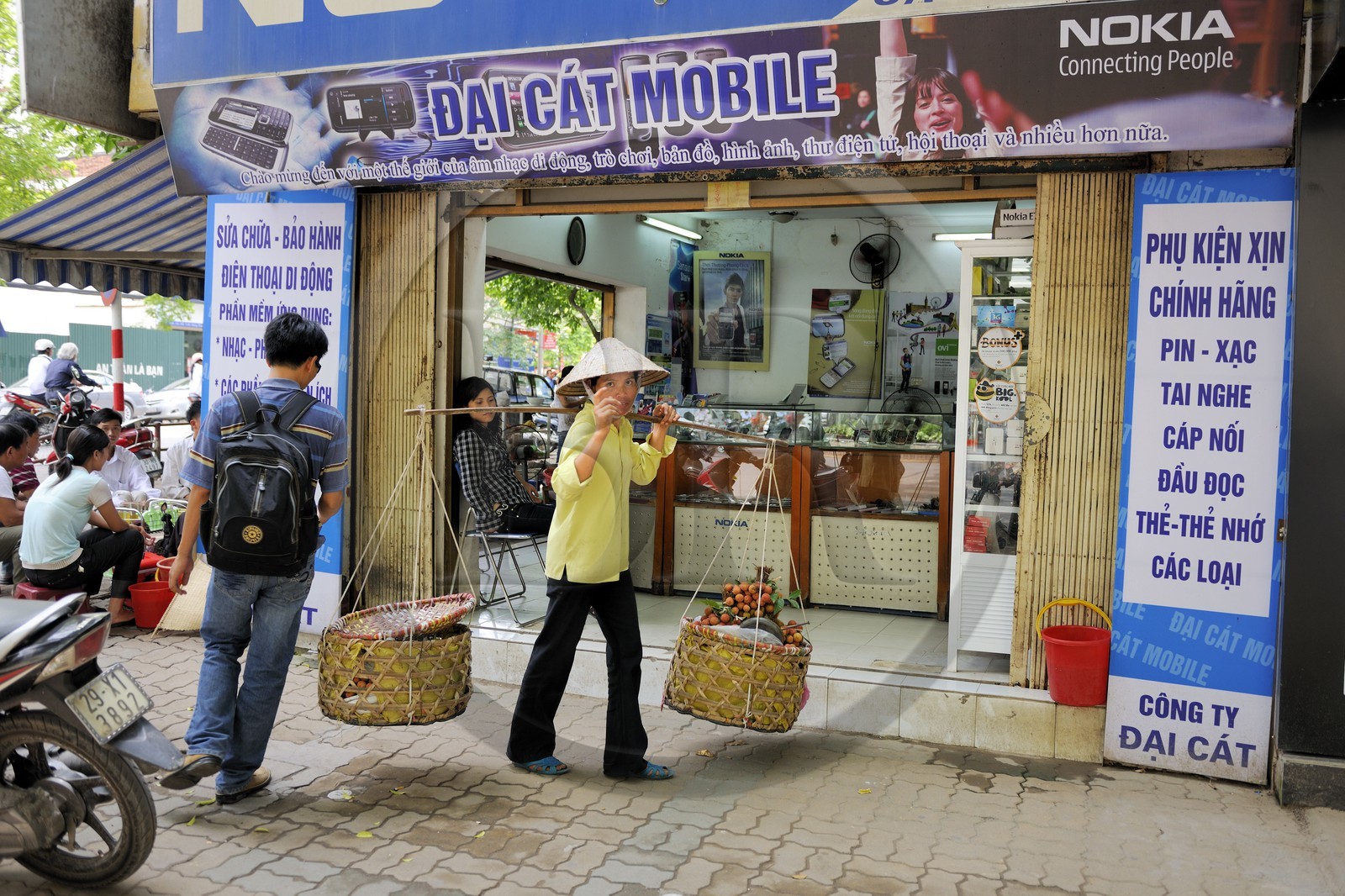 Vietnam, Hanoï, vieille ville, marchande de fruits (lychee) avec sa palanche devant une boutique de téléphones mobiles