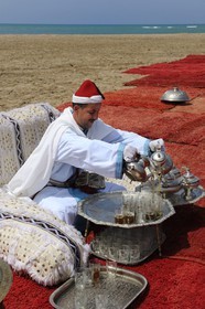 Morocco, Oriental Region, man in ceremonial cloth serving mint tea on the beach