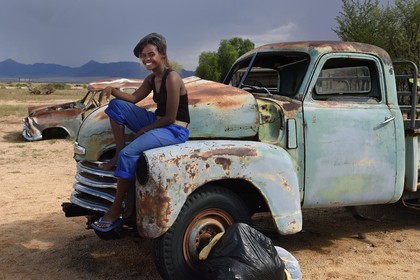 Namibia, Khomas Region, Namib Desert East of the Namib Naukluft National Park, at Solitaire petrol station, Gloria a young Namibian backpacker sitting on a dumped Chevrolet pickup
