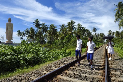 Sri Lanka, Province du Sud, region de Galle, Telwatta, écoliers marchant sur la voie ferrée de Colombo à Galle devant le Bouddha de Peraliya en memoire des nombreuses victimes du train bondé emporté par le Tsunami du 26 décembre 2004