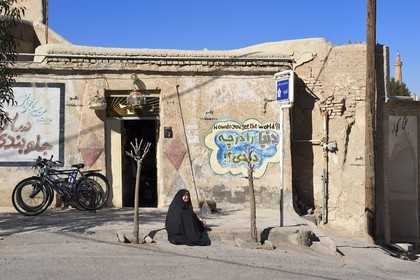 Iran, Isfahan province, Dasht-e Kavir desert, city of Nain also known as Naein, woman in front of a house with graffiti showing how do you see the world
