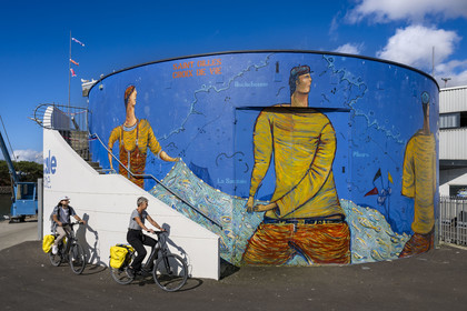 France, Vendée (85), Saint-Gilles-Croix-de-Vie, cyclistes passant devant la peinture murale sur la facade de la criée réalisée par Manou Feustay