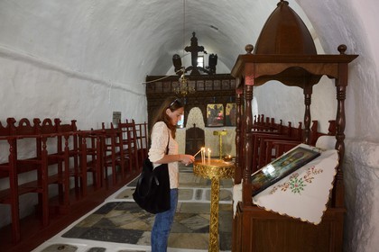 Greece, Cyclades islands, Mykonos island, Chora (Mykonos town), a young woman lights a candle in the chapel of Saint Nicolas district