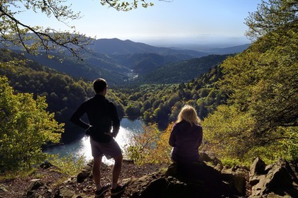 France, Haut Rhin, Ballons des Vosges Regional Natural Park, Rimbach pres Masevaux, hiker walking on the GR5 hiking trail over the Lac des Perches, the plain of Alsace and the Alps in the background