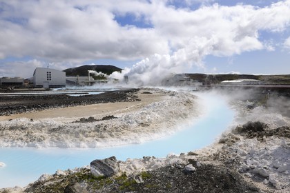 Iceland, Sudurnes Region, Grindavik, the Blue Lagoon with drains and lava in the foreground and the geothermical factory in the background