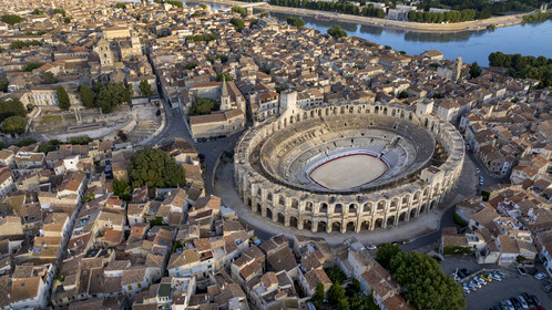 France, Bouches du Rhone, Arles, the Arena, a Roman amphitheater built around 80-90 AD, and the ancient theatre from the 1st century BC on the left, listed as World heritage by UNESCO, in the heart of the old town and the Rhone river in the background (aerial view)
