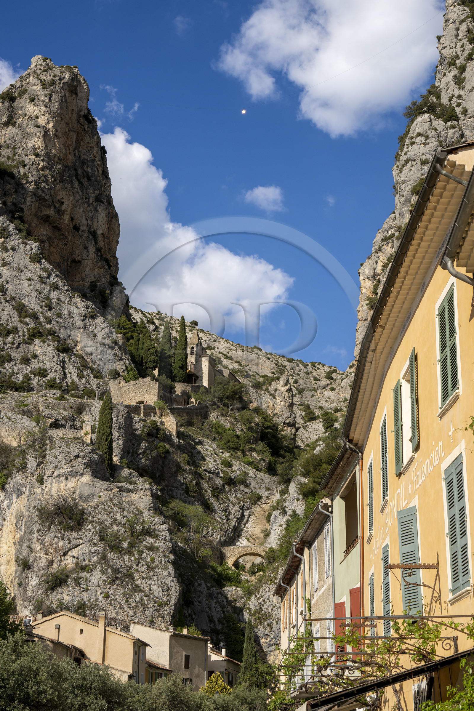 France, Alpes-de-Haute-Provence (04), Parc Naturel Régional du Verdon, Moustiers-Sainte-Marie, labellisé Les Plus Beaux Villages de France,l'Etoile de Moustier accrochée à une chaîne à plusieurs dizaines de mètres au-dessus du sol et la chapelle Notre-Dame de Beauvoir en arrière plan dans la falaise