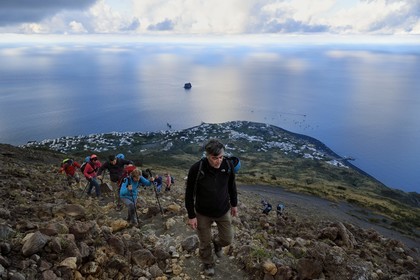 Italie, Sicile, iles Eoliennes, classées Patrimoine Mondial de l'UNESCO, ile de Stromboli, randonneurs dans l'ascension du volcan, le village de Stromboli et l'ilot de Strombolicchio en arrière plan