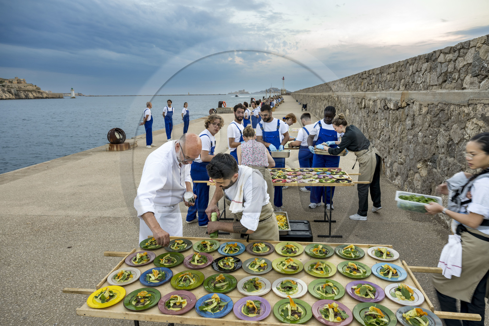 France, Bouches-du-Rhône (13), Marseille, Zone Euroméditerranée, grand port maritime de Marseille (GPMM), la digue du large, convives attablés à une grand table de banquet dressée par le chef Emmanuel Perrodin dans le cadre des Diners Insolites, derniers préparatifs au plats France, Bouches-du-Rhône (13), Marseille, Zone Euroméditerranée, grand port maritime de Marseille (GPMM), la digue du large, convives attablés à une grand table de banquet dressée par le chef Emmanuel Perrodin dans le cadre des Diners Insolites, derniers préparatifs au plats
