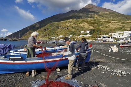 Italie, Sicile, iles Eoliennes, classées Patrimoine Mondial de l'UNESCO, ile de Stromboli, le pecheur Gaetano Cusolito réparant ses filets sur la plage de Scari et le volcan du Stromboli en arrière plan