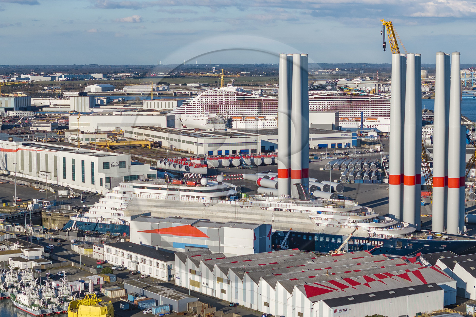 France, Loire-Atlantique (44), Saint-Nazaire, le chantier du super-yacht de luxe Ritz-Carlton Luminara dans la forme Joubert au premier plan, les tours d'éoliennes sont stockées avant embarquement, le paquebot de 333m MSC World America construit par les Chantiers de l'Atlantique en arrière plan (vue aérienne)