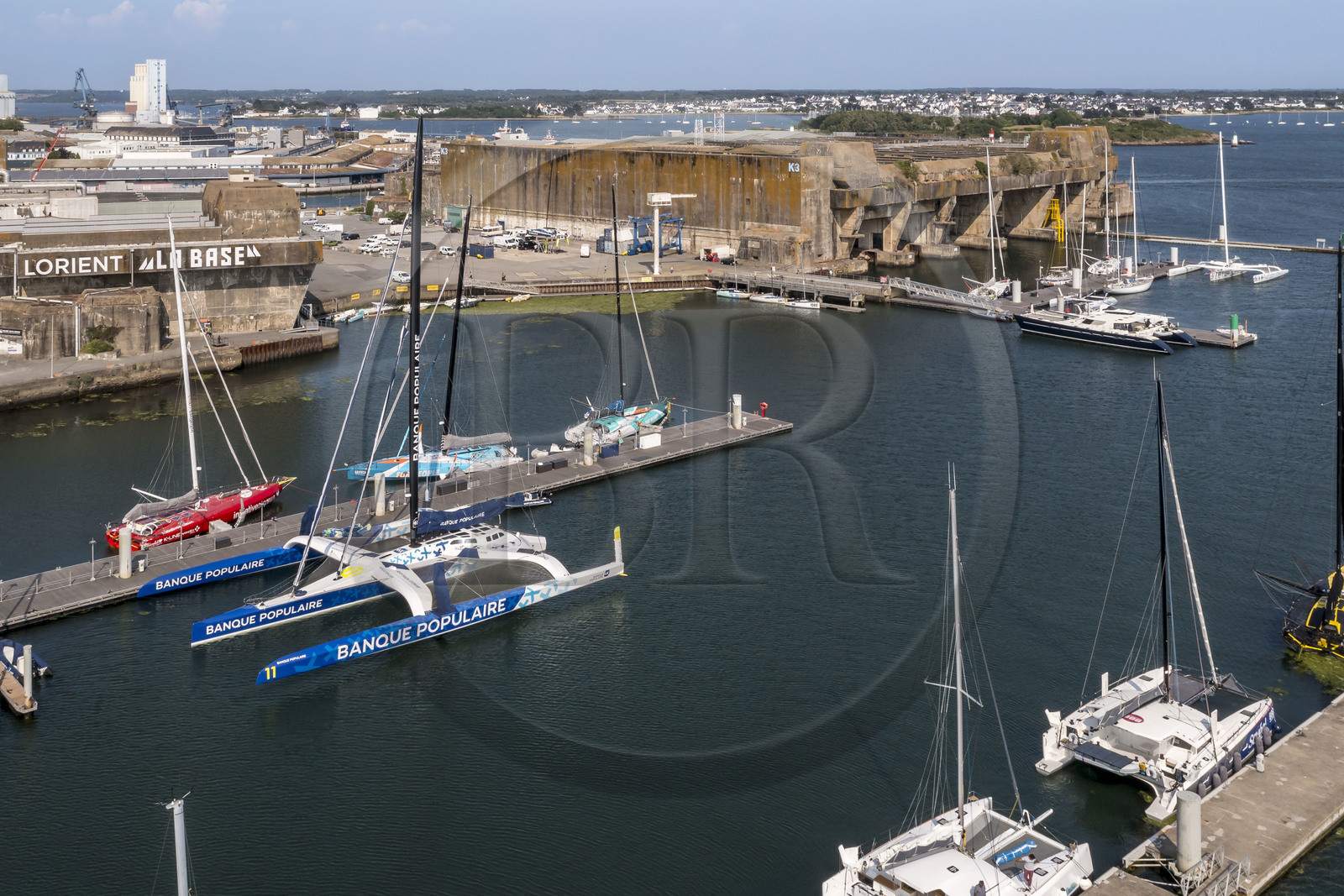 France, Morbihan (56), Lorient, le port de Lorient La Base dans l'ancienne base de sous-marins construite par les Allemands, il est conçu et équipé de façon à accueillir les professionnels du nautisme, les événements nautiques et les grandes unités telles que les monocoques et les multicoques de la Course au Large, voilier maxi-trimaran-hydroptère Maxi Banque populaire XI du navigateur Armel Le Cléac'h (vue aérienne)