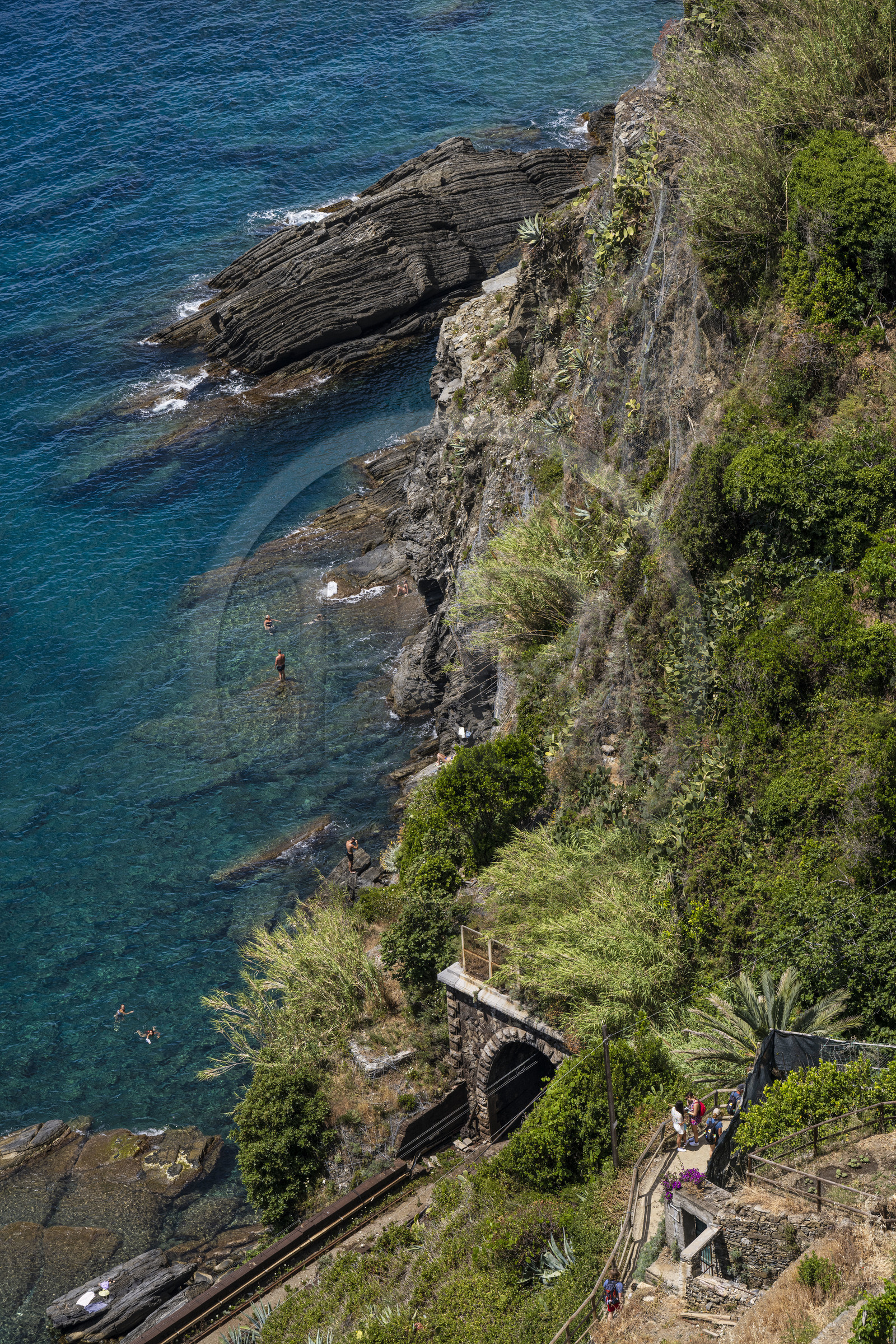 Italy, Liguria, Cinque Terre National Park listed as World Heritage by UNESCO, village of Vernazza, hikers on the GR 592 coastal path overlooking the railway line and swimmers at the foot of the cliffs